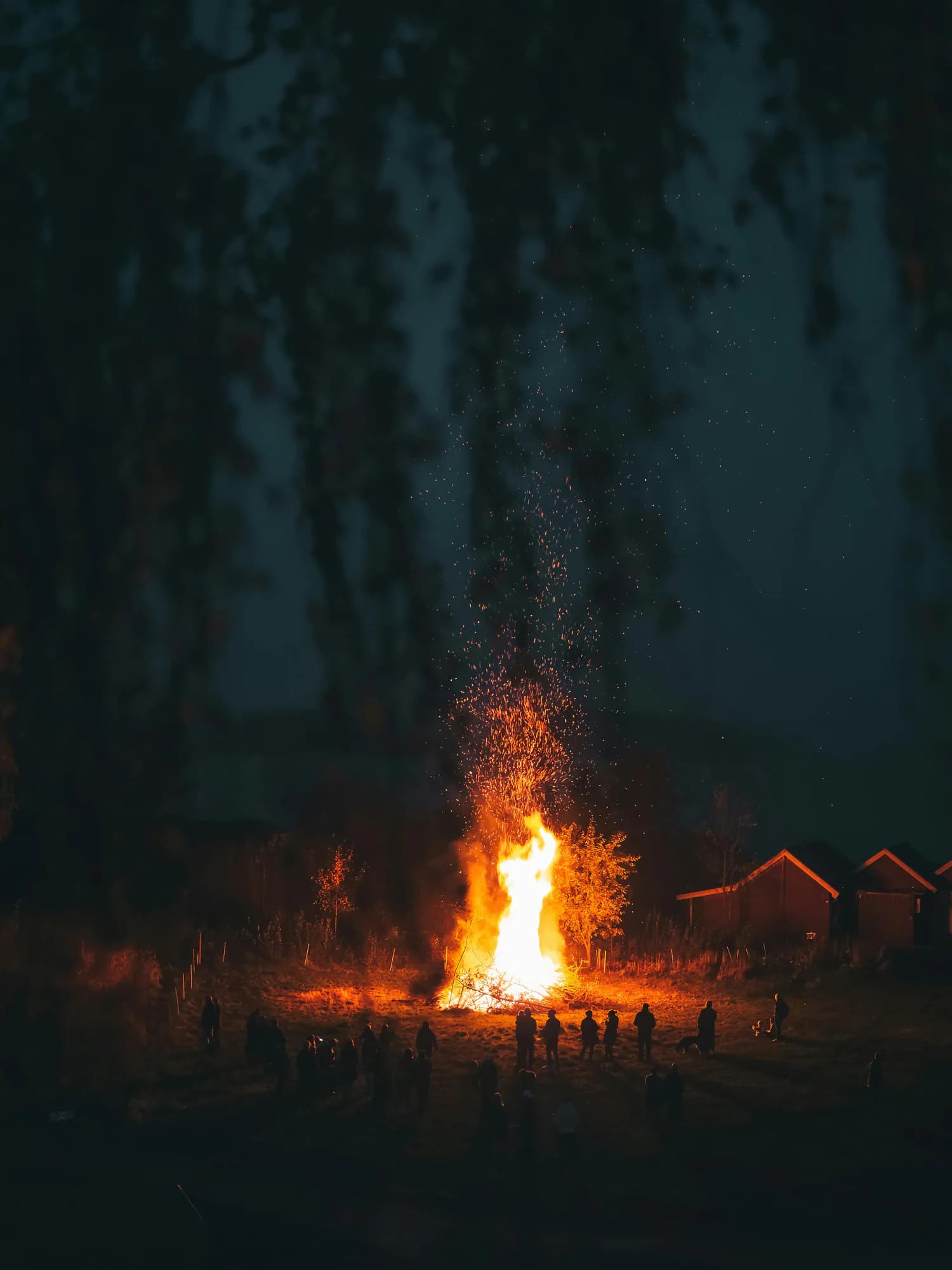 A campfire throwing sparks into the night sky, guests gathered around it