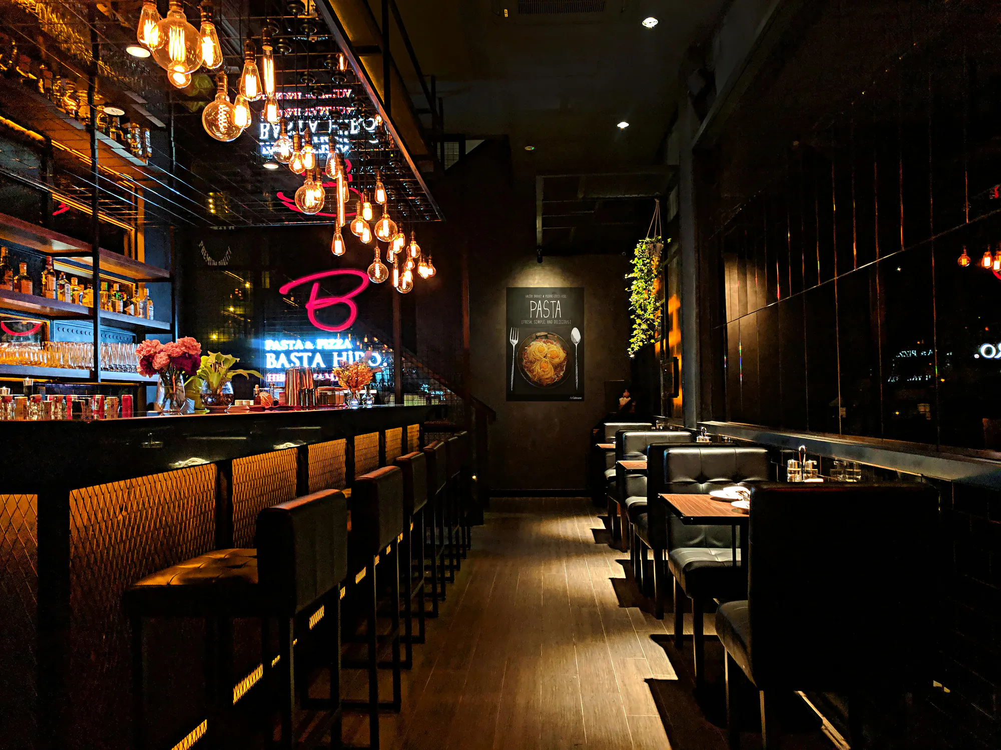 A dim lounge with a long bar, pendant lights and leather booths