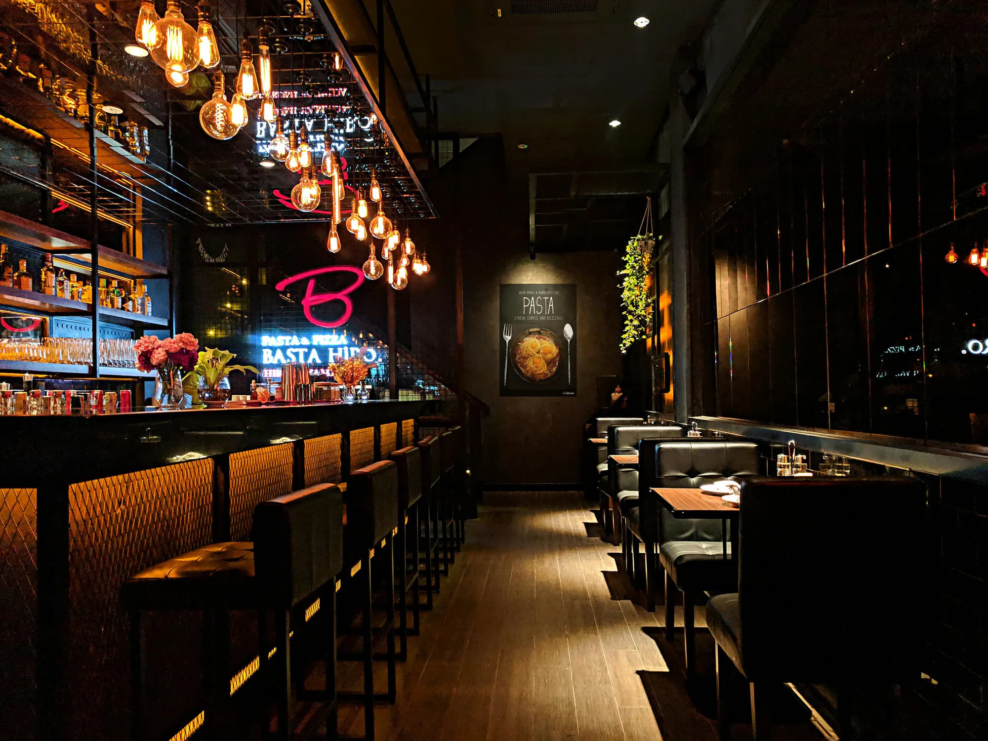 A dim lounge with a long bar, pendant lights and leather booths