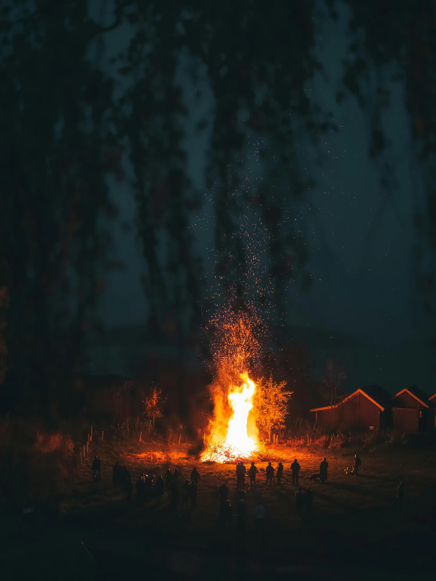 A campfire throwing sparks into the night sky, guests gathered around it